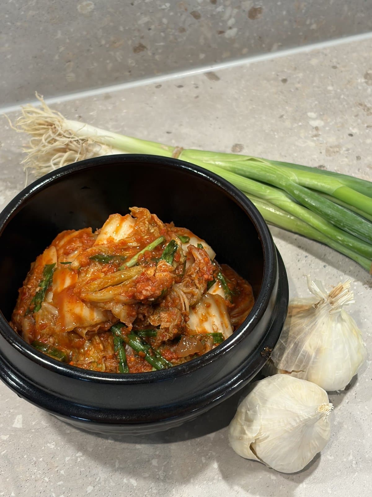 Vår kimchi i en svart skål med salladslök och vitlök